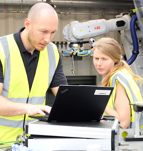 Two people operating a PC in front of a shipping container with a ABB robot